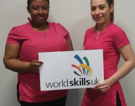 Two female beauty students in pink uniform with World Skills sign