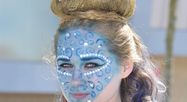 Hair show model with purple flowers in hair and blue makeup