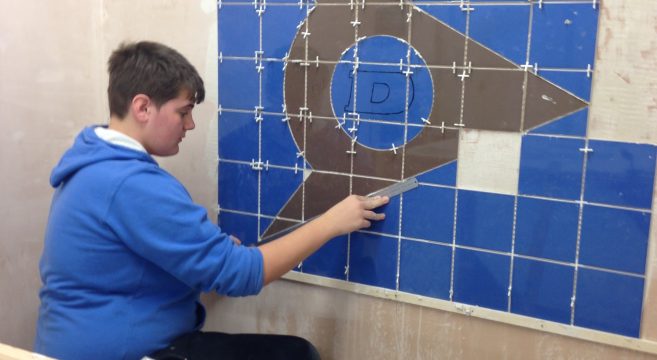 Male student measuring blue and grey tiles