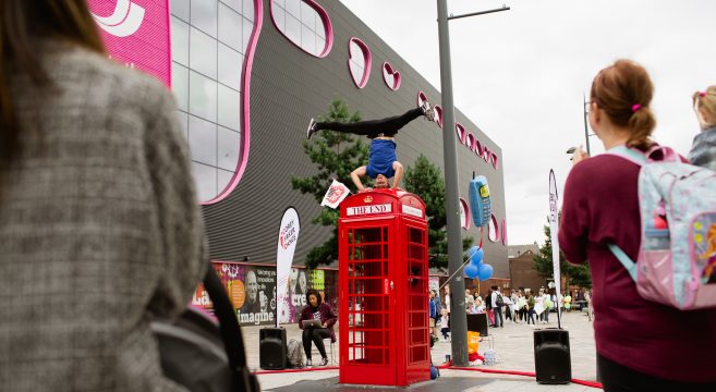 Acrobat standing on head on top of red phone box