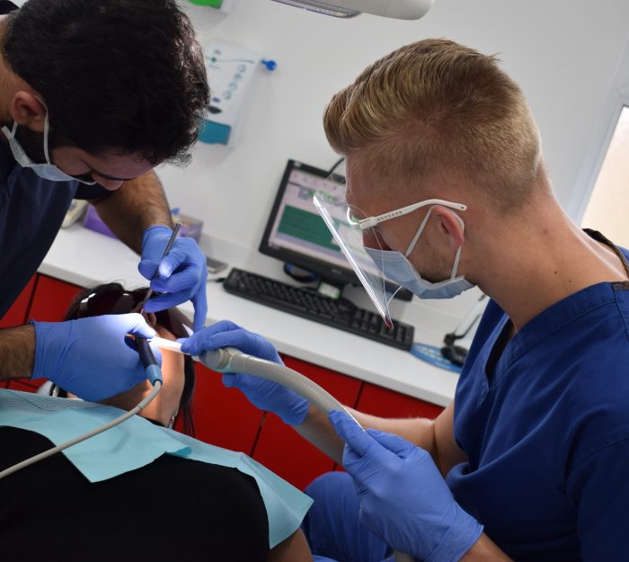 Male dental nurse apprentice assisting dentist with patient's treatment
