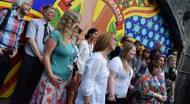 Group of students and staff member pictured in front of a mural