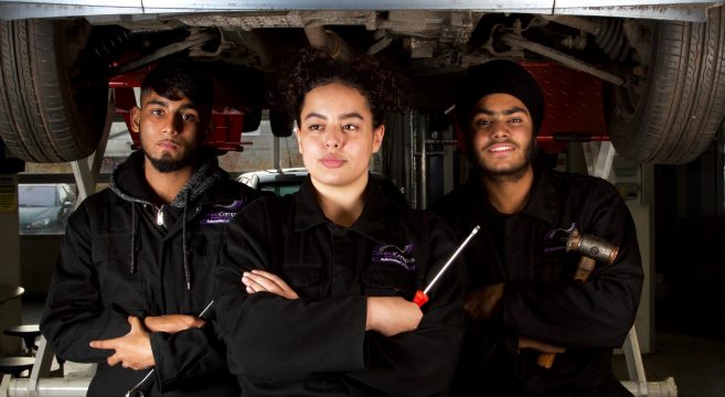 Group of automotive students with equipment in their hands pictured underneath a car