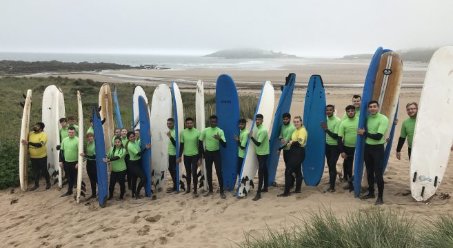 Students pictured on a beach with surfboards