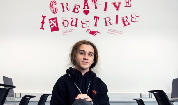 Digital & Creative Media male student sitting under Creative Industries sign