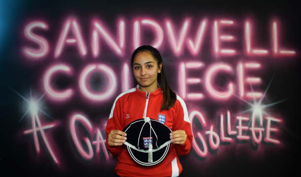 Sport student holding her England cap in front of Sandwell College mural