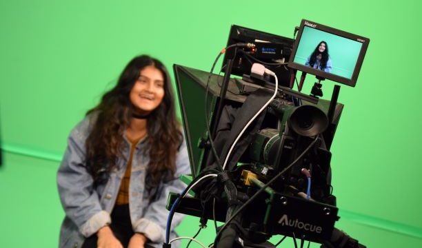 Student being filmed by TV camera in front of a green screen