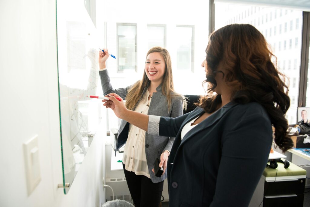 Two ladies discussing and using a whiteboard