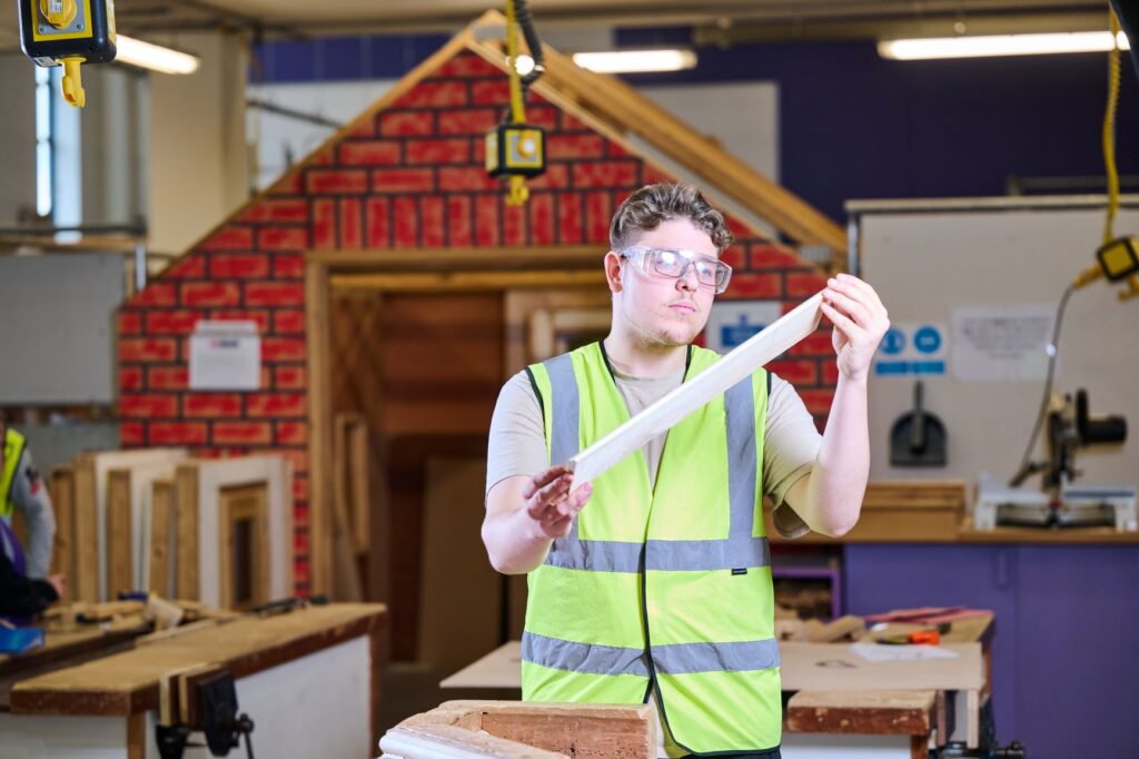 Carpentry student in hi-vis vest and safety glasses holding piece of wood