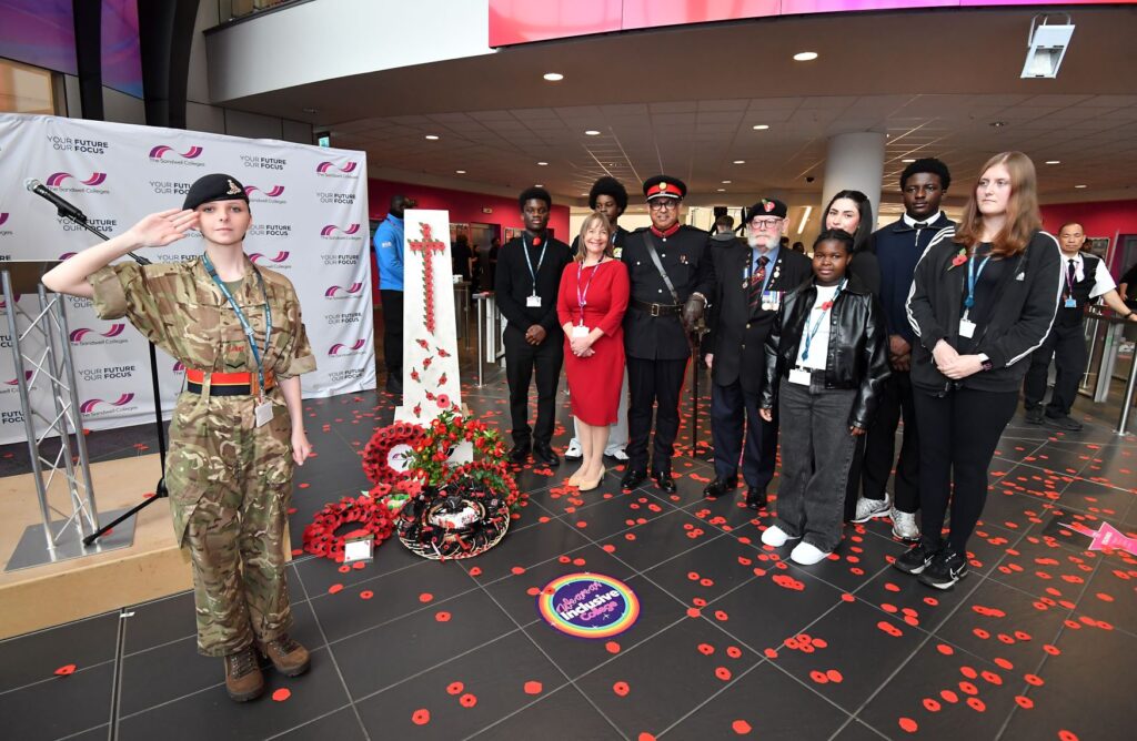 Army cadet student salutes at the cenotaph next to staff, students and visitors