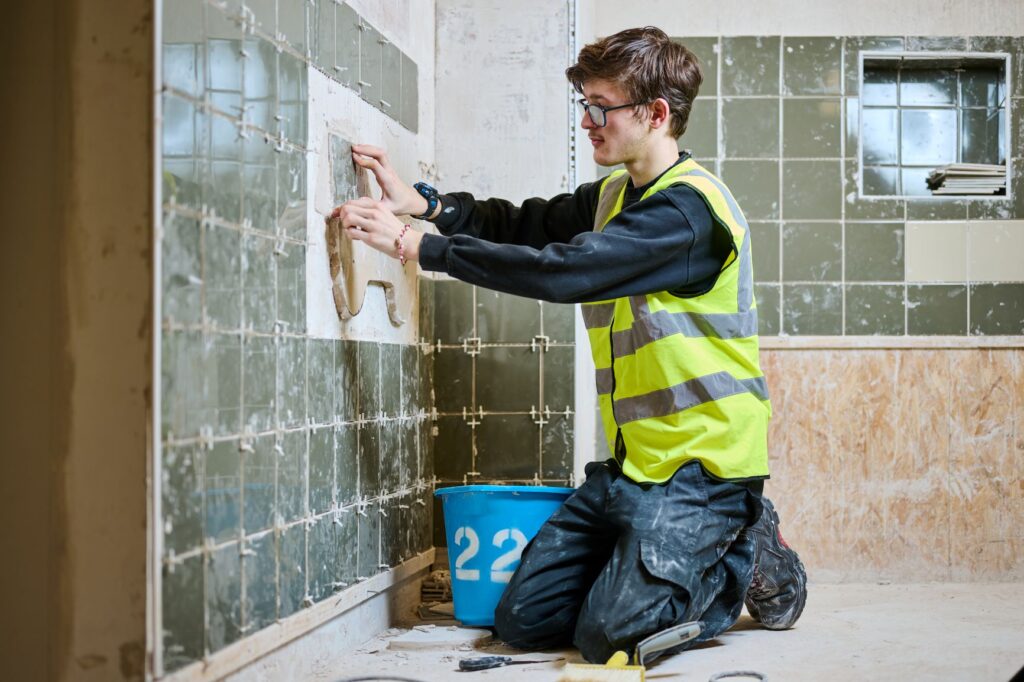 Student in hi-vis vest tiling wall