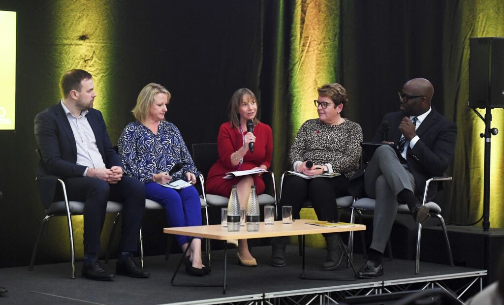 Five panel members speaking with college principal Lisa Capper with microphone