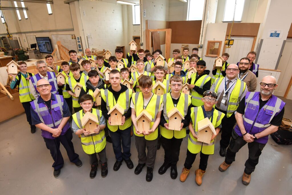 College staff with school students wearing hi vis holding bird boxes